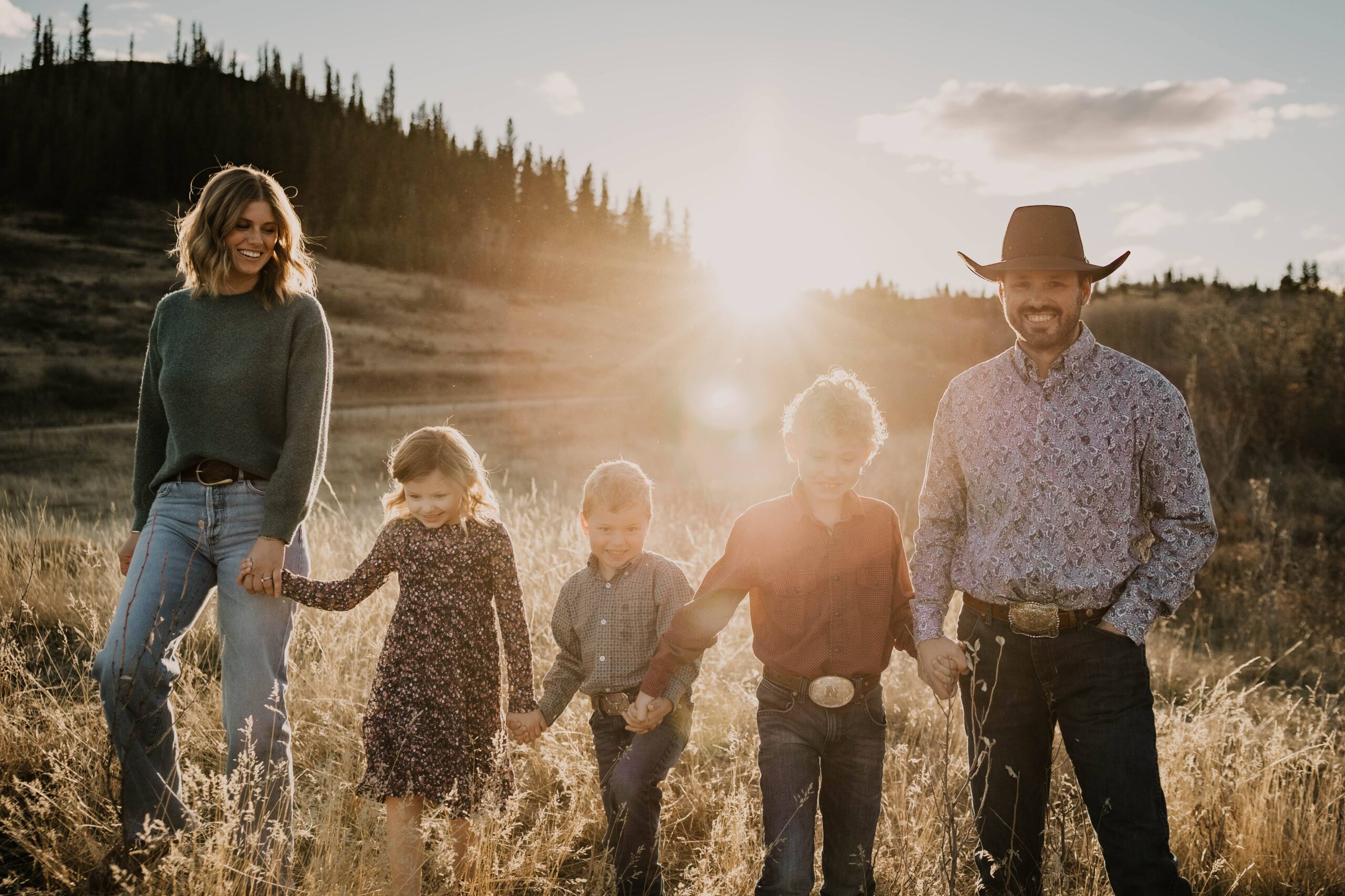 cowboy family walks hand in hand through their saskatchewan pasture at sunset