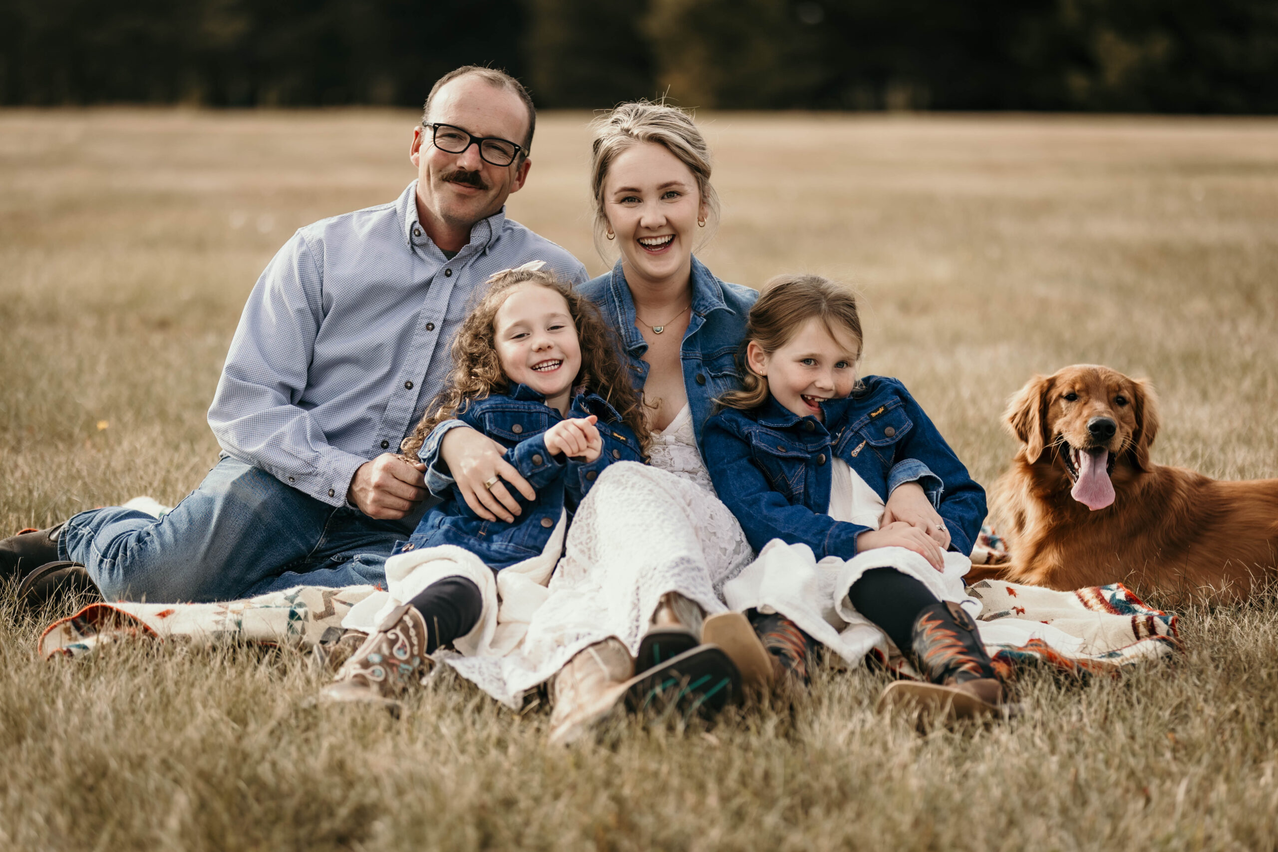 Family with dog cuddle and smile at the camera during a fall mini photo session in Medicine Hat Alberta