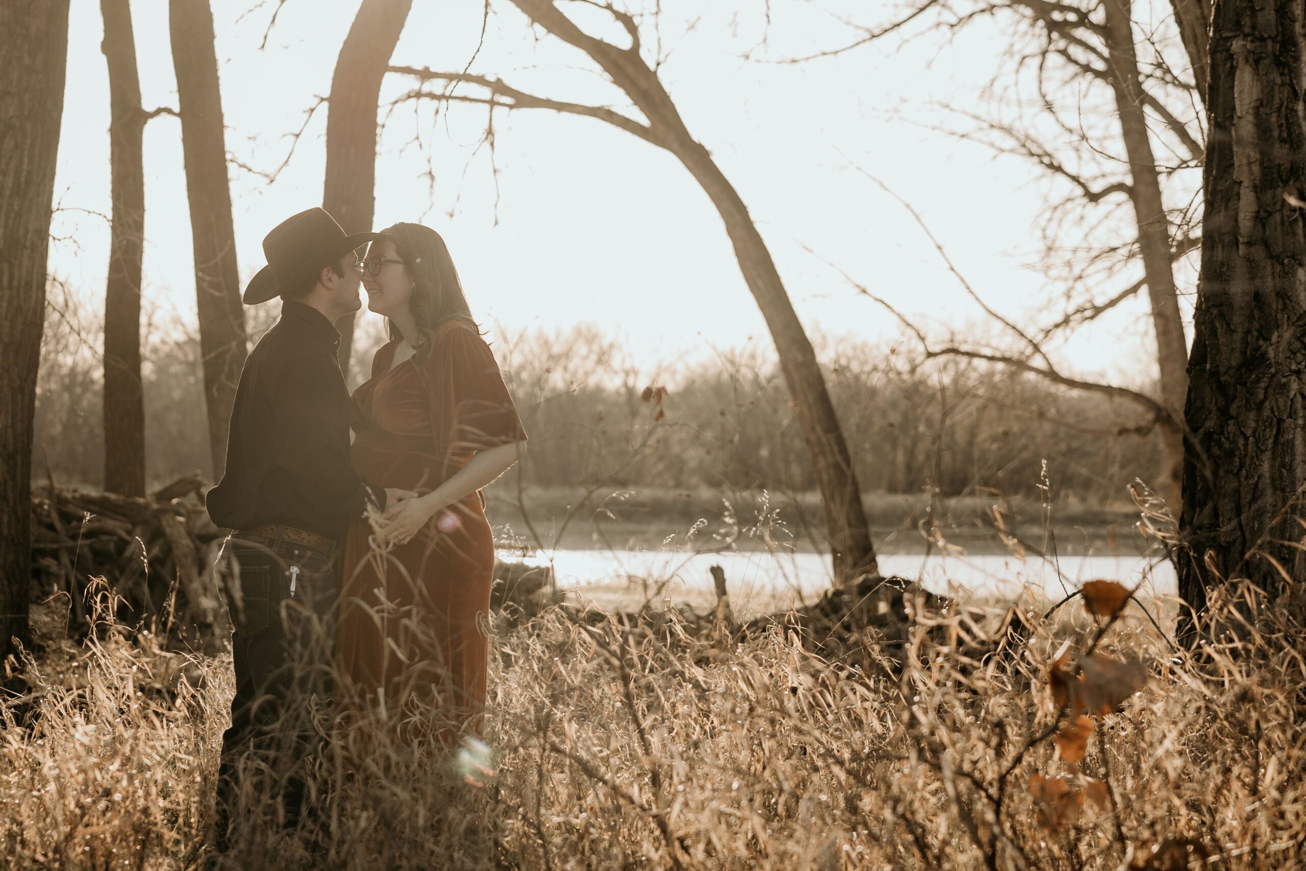 couple embrace in the tall grass by a river during a maternity photo shoot in medicine hat alberta